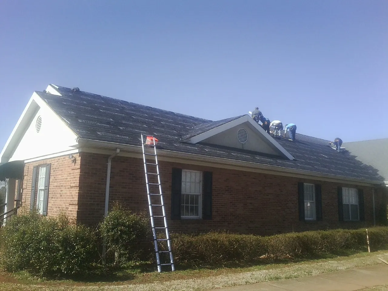 Crew tearing shingles off a brick ranch roof with a ladder set — Emergency Roof Repair work by our crew in Falkland