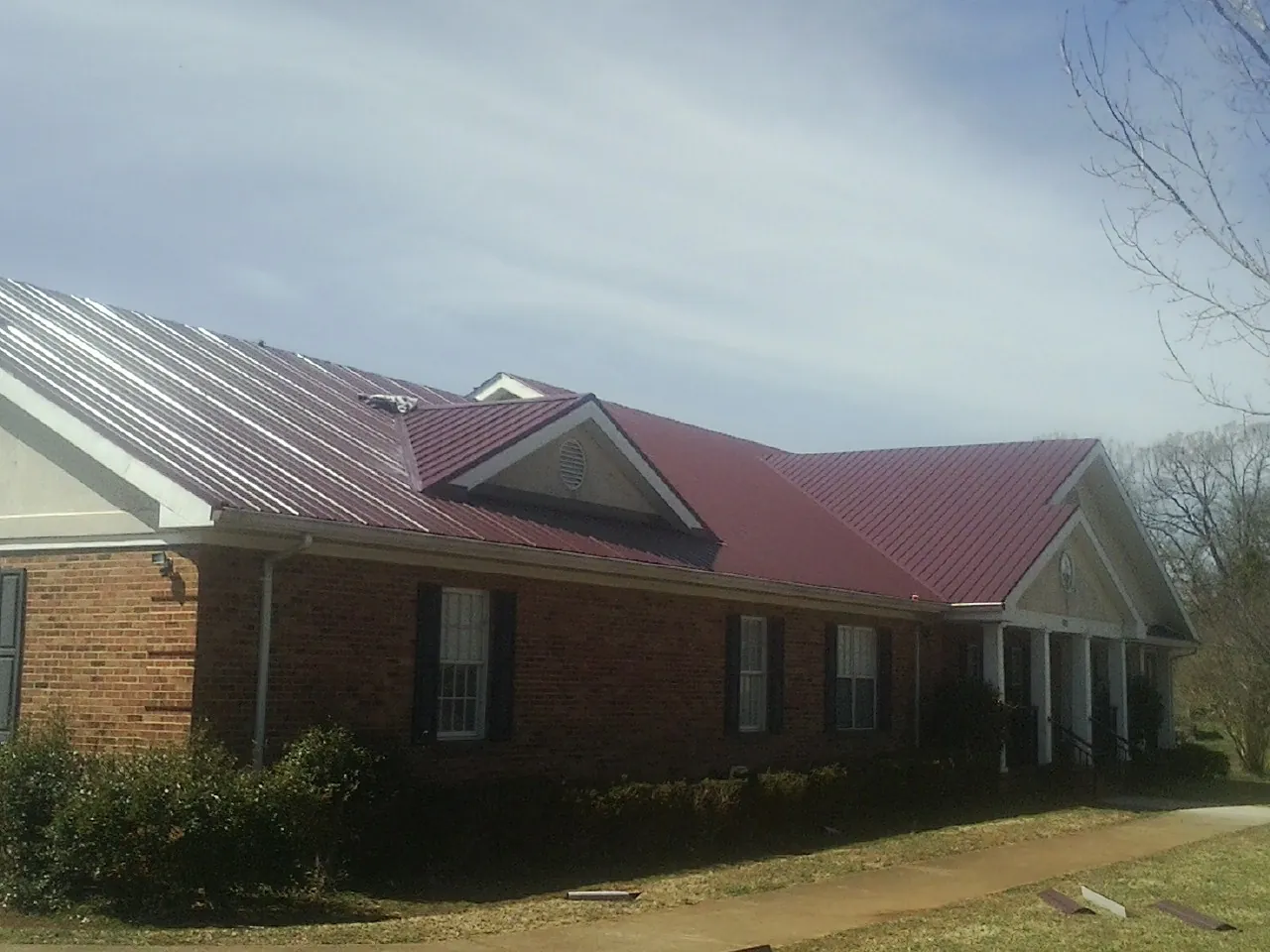 Red metal roof with gabled entries on a long brick building, from a Hail Damage Roof Repair job in Falkland