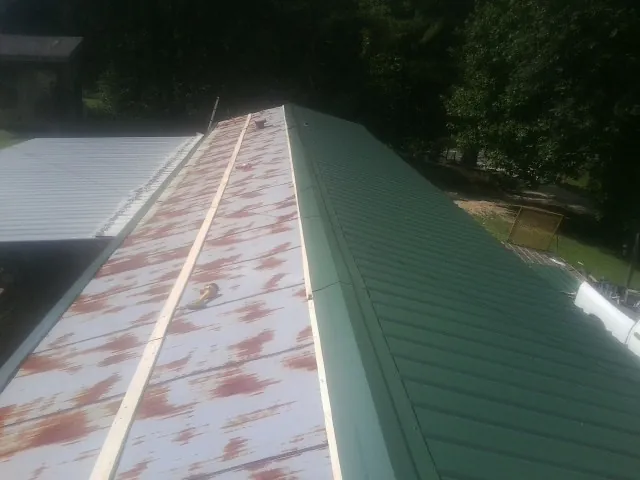 Old rusted panels beside newly installed green metal roofing — Wind Damage Roof Repair by Roofing Brothers in Falkland