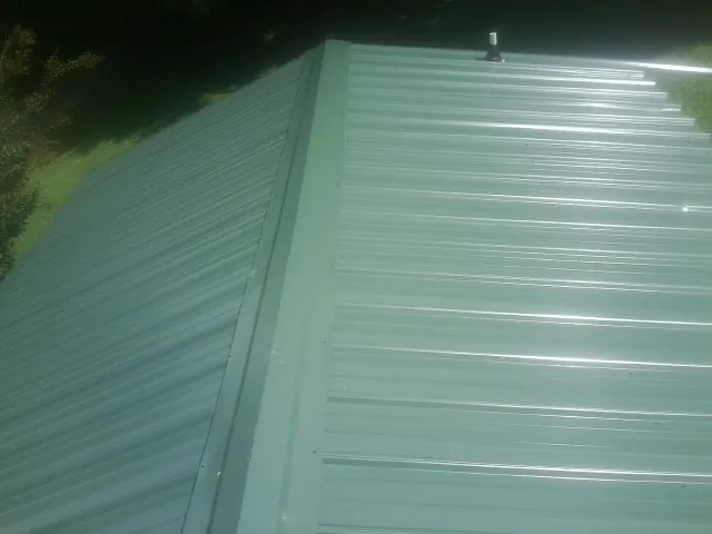 New green metal panels meeting at the ridge of a roof — Flat Roof Repair work by our crew in Falkland