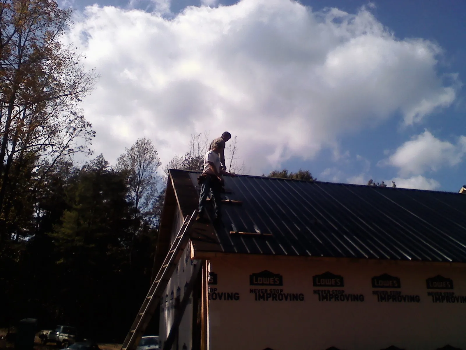 Roofer fastening dark metal panels high against a cloudy sky, from a Roof Inspection job in Falkland