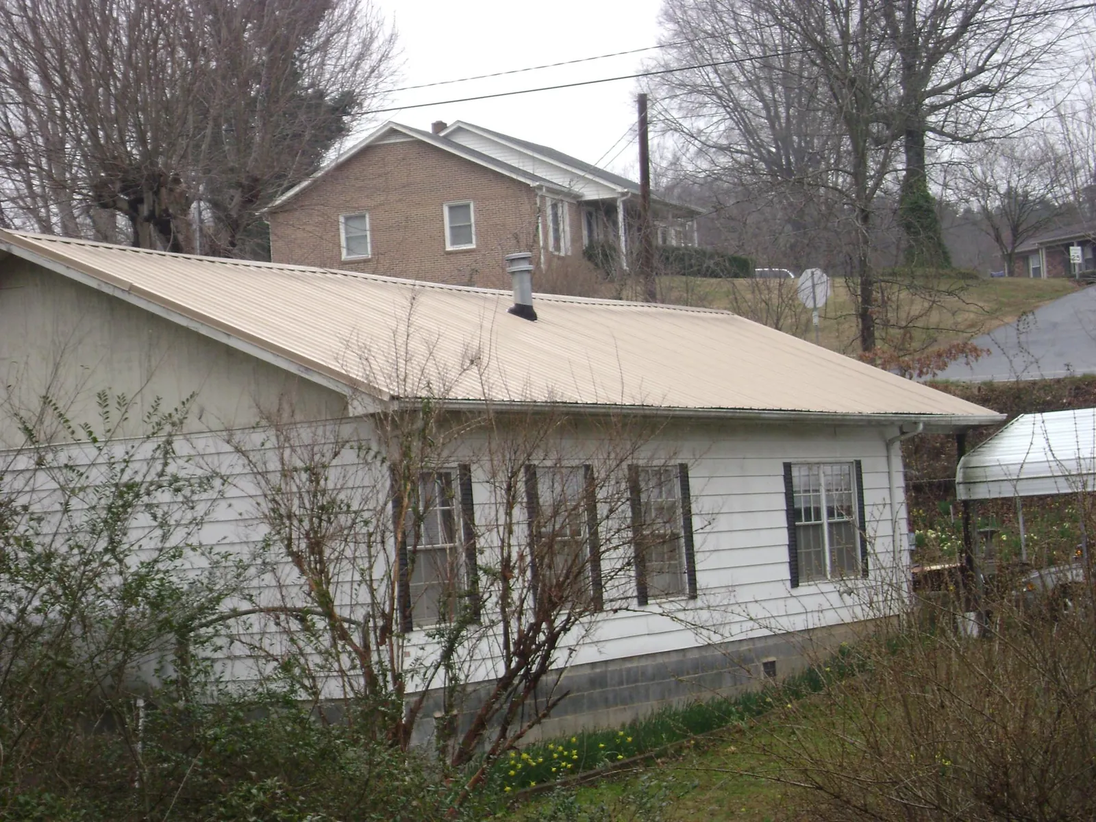 Tan metal roof on a white sided house set into a hillside — Commercial Roofing by Roofing Brothers in Falkland